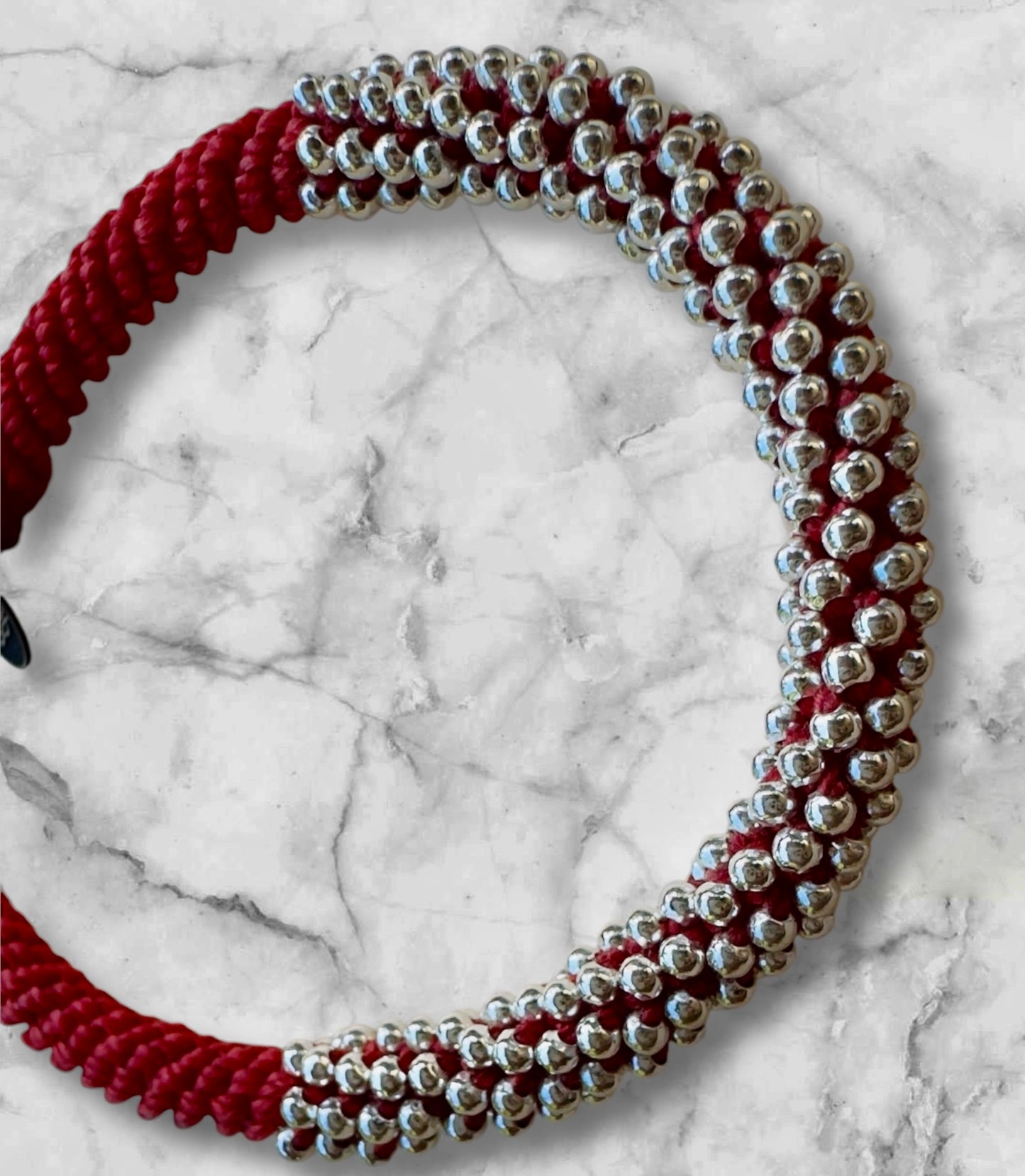 Rotes Makramee-Armband mit 240 kleinen Silberperlen, fotografiert auf weißem Marmorhintergrund – handgefertigt und detailreich.