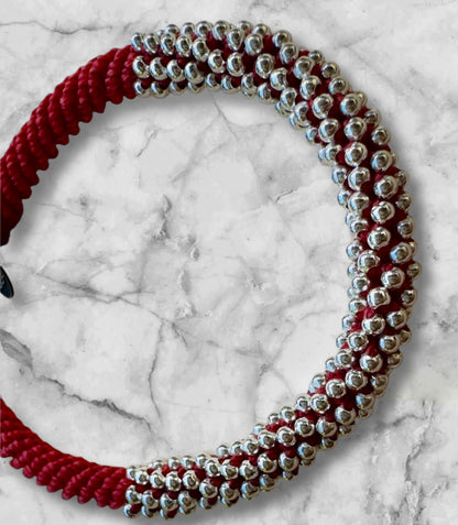 Rotes Makramee-Armband mit 240 kleinen Silberperlen, fotografiert auf weißem Marmorhintergrund – handgefertigt und detailreich.
