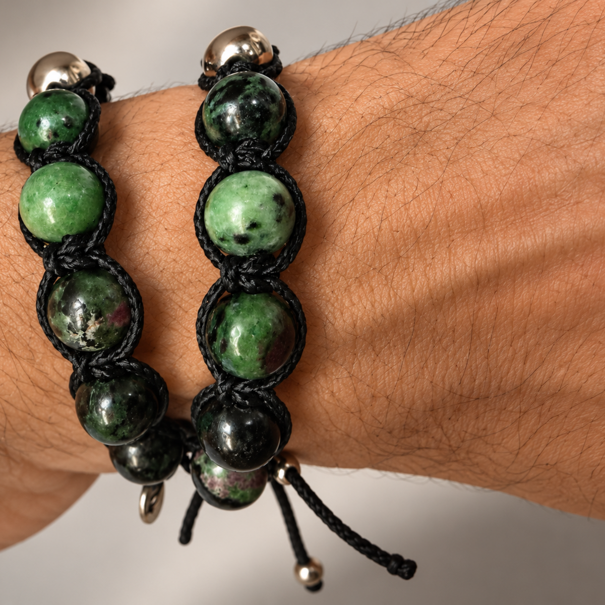 Zwei NEXO ANYOLIT Armbänder am Handgelenk: Nahaufnahme der grün-schwarz gemusterten Rubin-Zoisit-Perlen, schwarzen Makrameeknoten und Silberdetails.